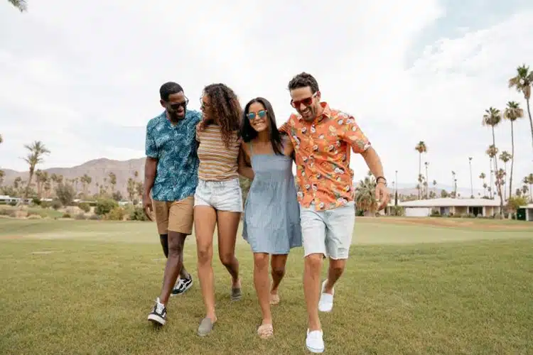 Four traveler friends walking with arms around one another on golf course