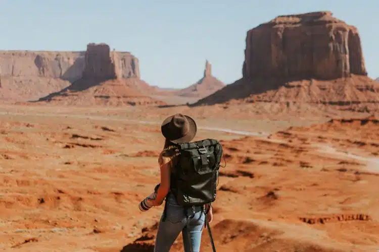 Adventurer stands in canyon holding camera looking at towers in the distance