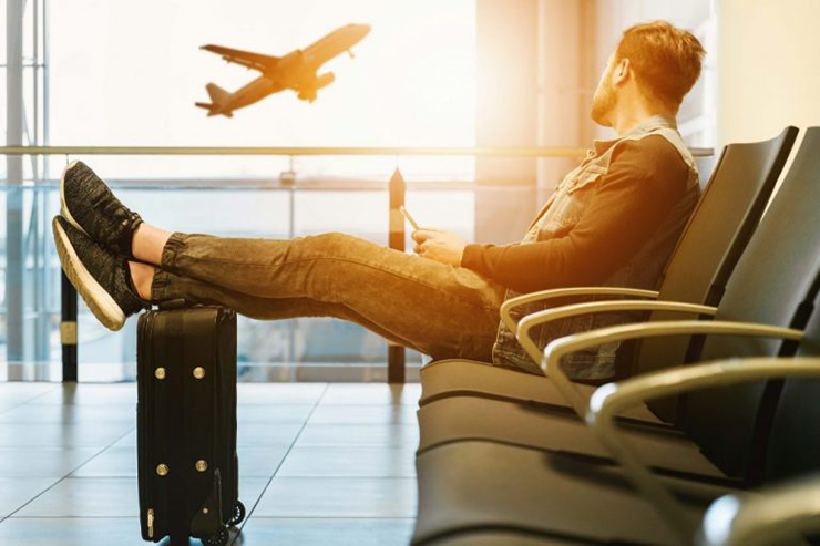 Traveler sitting in airport with feet resting on the bag watching airplane out window