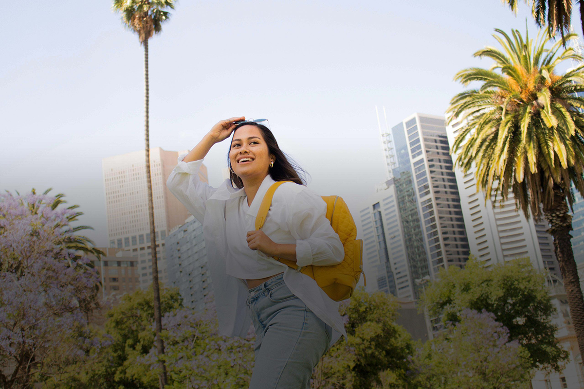 Traveler with yellow pack holding sunglasses in hand walking in the city