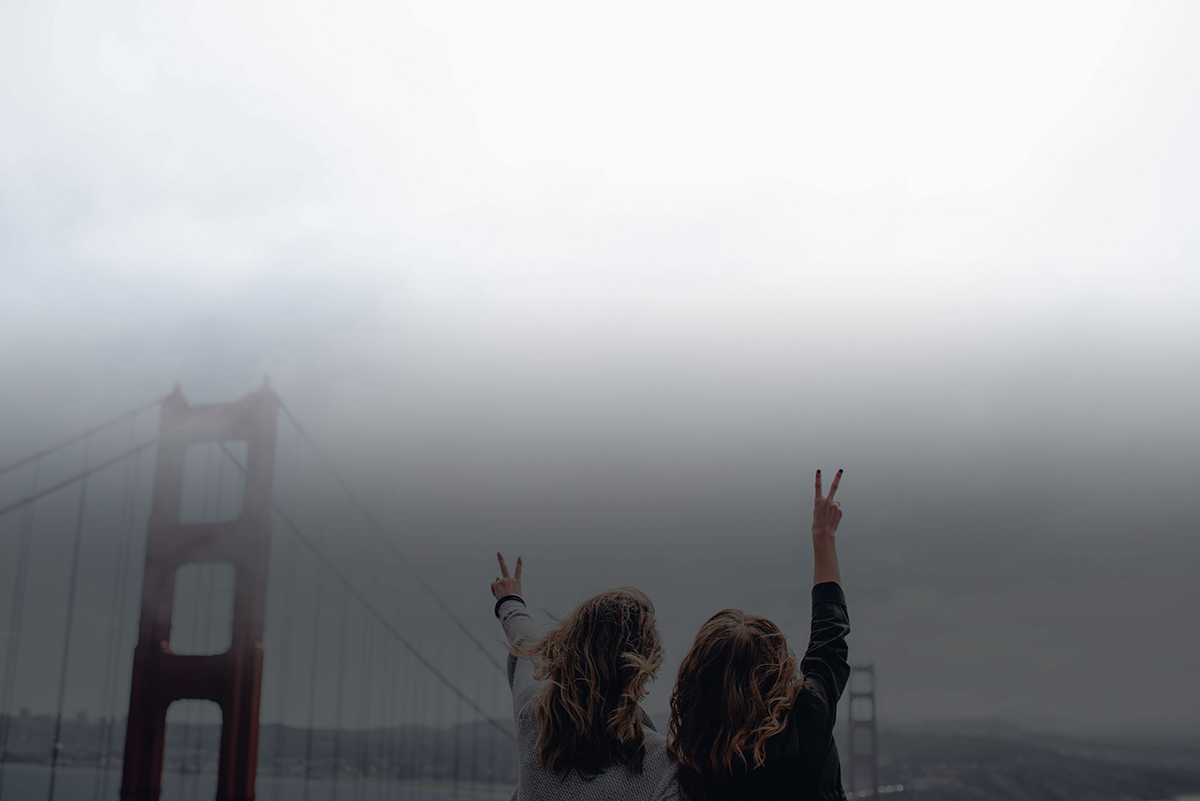 Two traveler friends in front of bridge holding hands raised above their heads