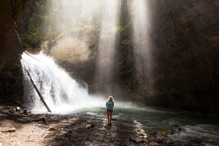 Woman standing next to a mountain waterfall in dim light