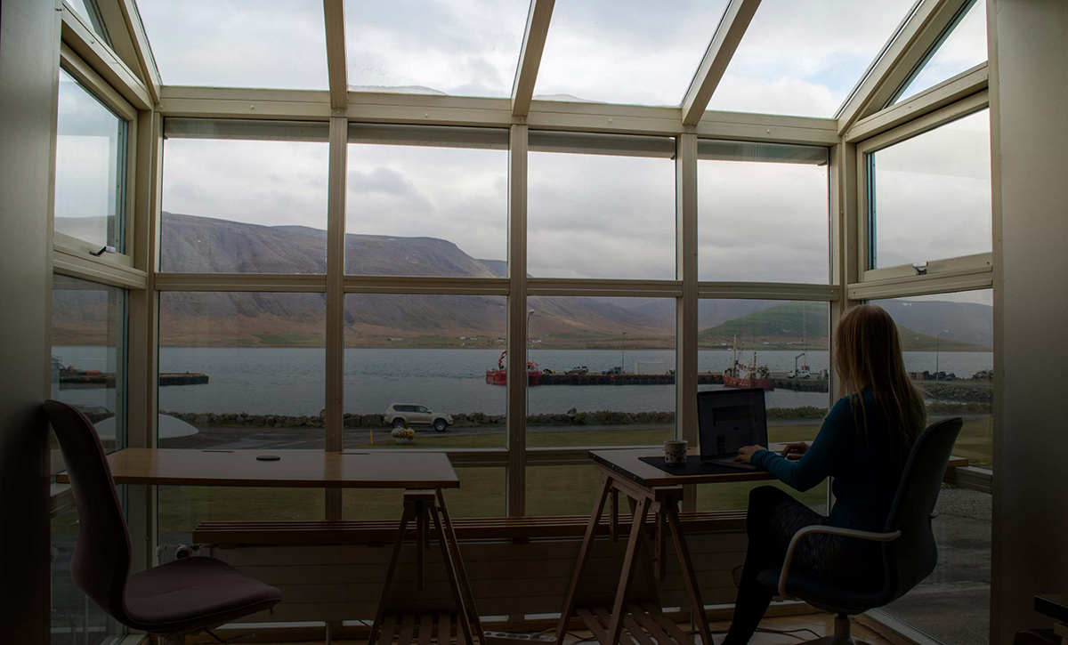 Person works remotely from laptop in front of window facing sea port