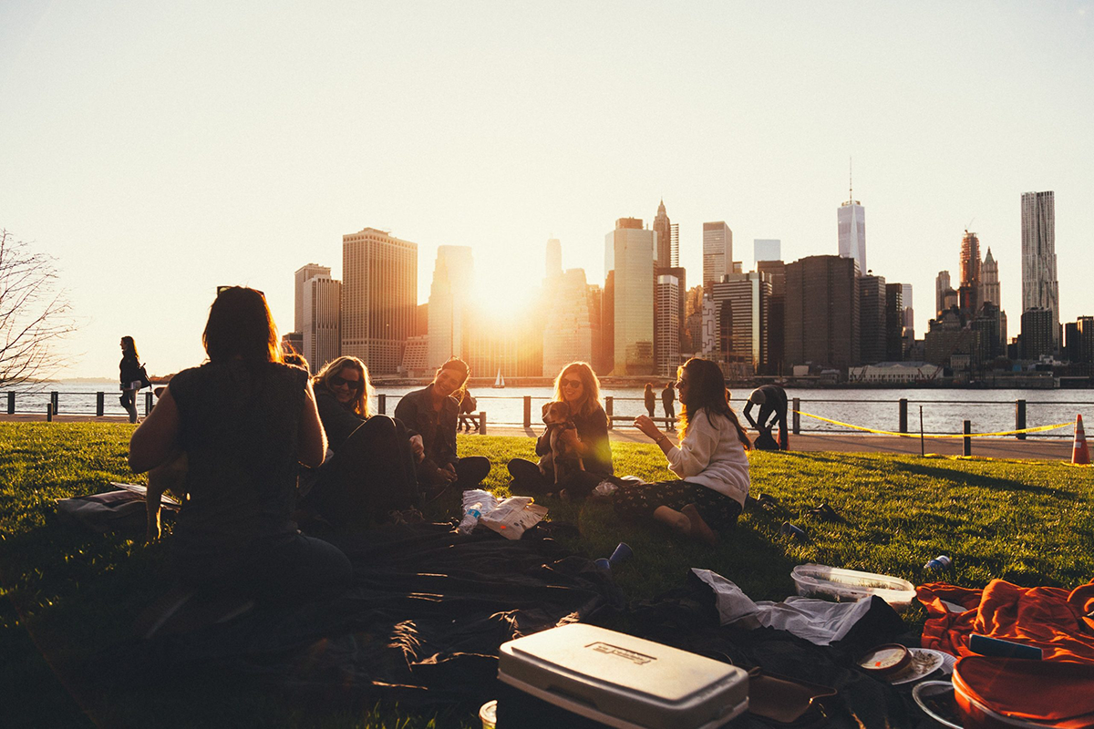 group of friends enjoying sunset by lake at the park