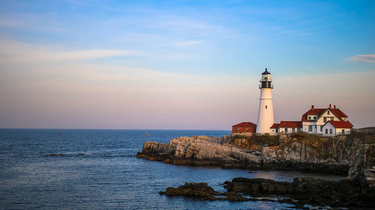 lighthouse pictured at edge of pier next to ocean with boats