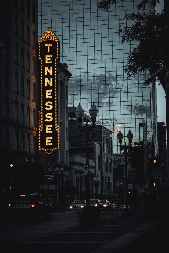 Street photo at night with cars driving past Tennessee sign downtown