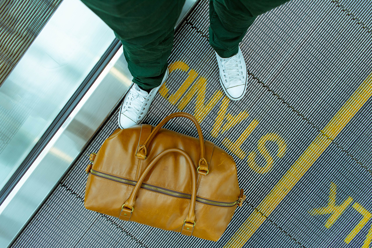 suitcase sitting on escalator next to person in green pants white shoes