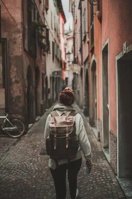 Traveler wearing backpack walks down cobble street alley