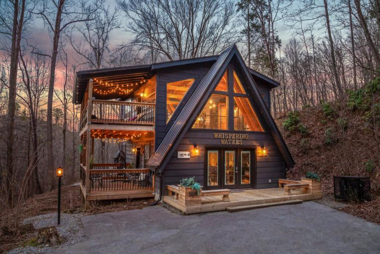 A-frame cabin with lights on inside and sunset in the background