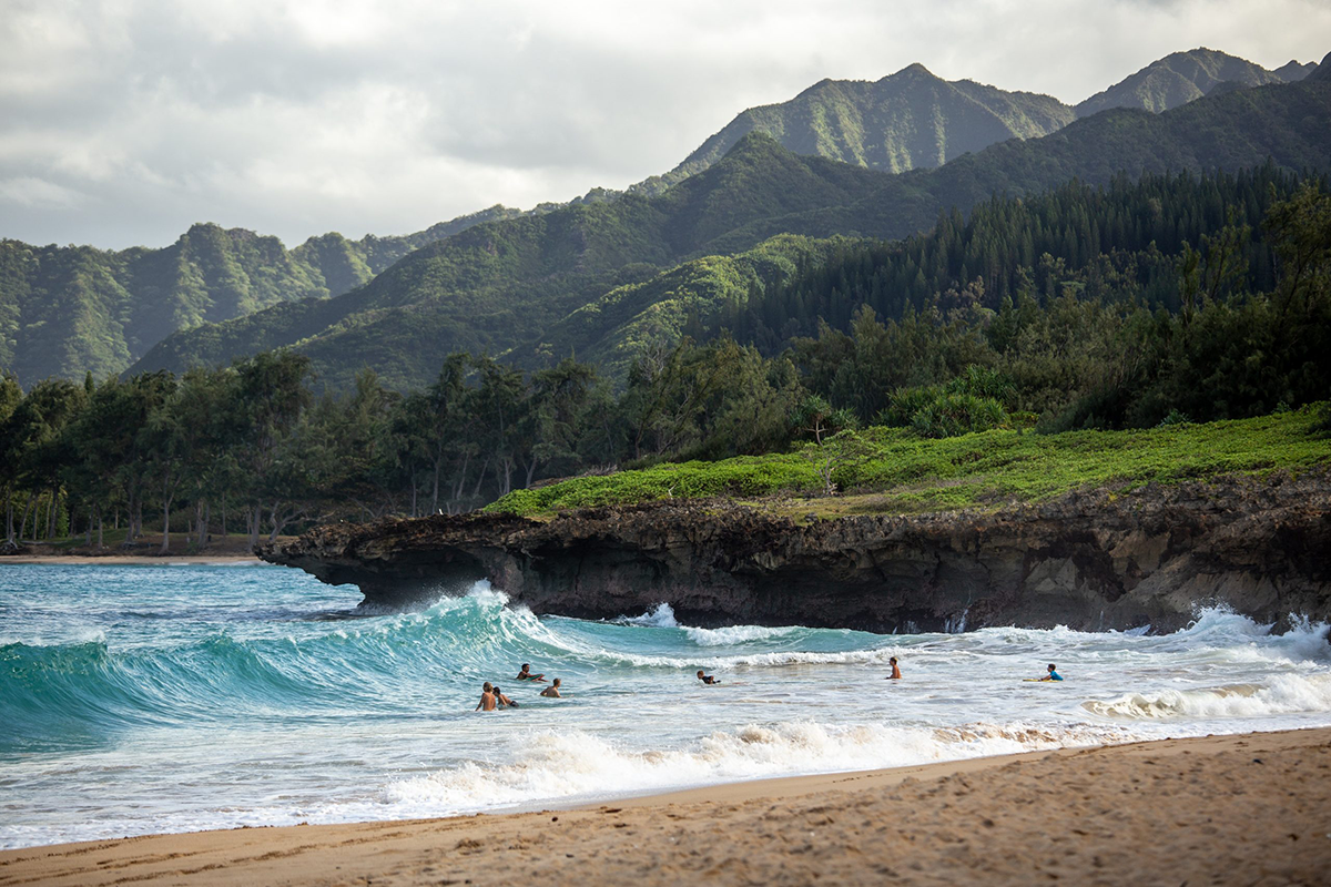 Molokai Hawaii is one of the perfect destinations to enjoy on Spring Break! This photo is a view of the beach in Hawaii with waves and rolling green hills in the background.