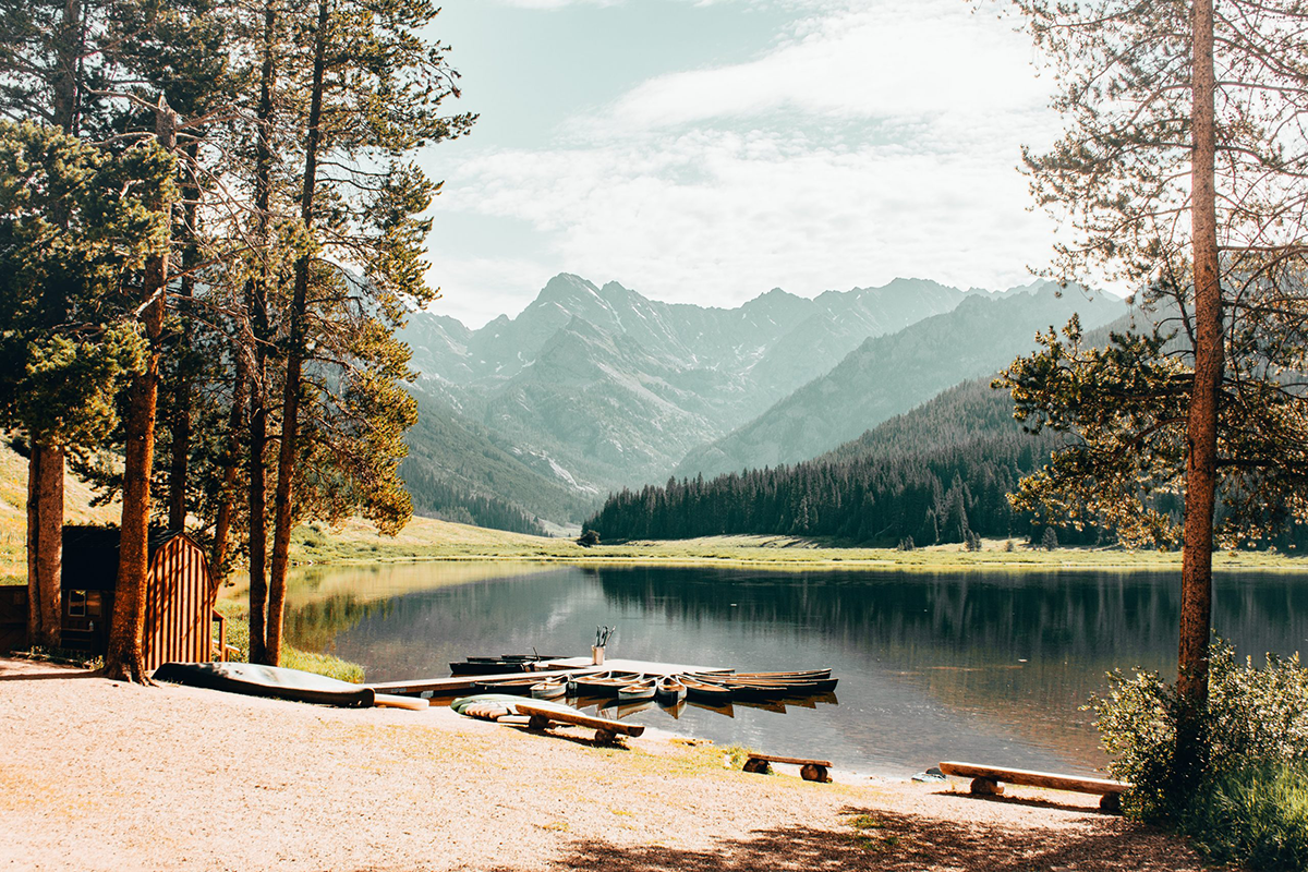 Ski towns are summer dream destinations for last minute travel. this is a photo of a ranch in vail colorado with a lake and the mountains in the background.