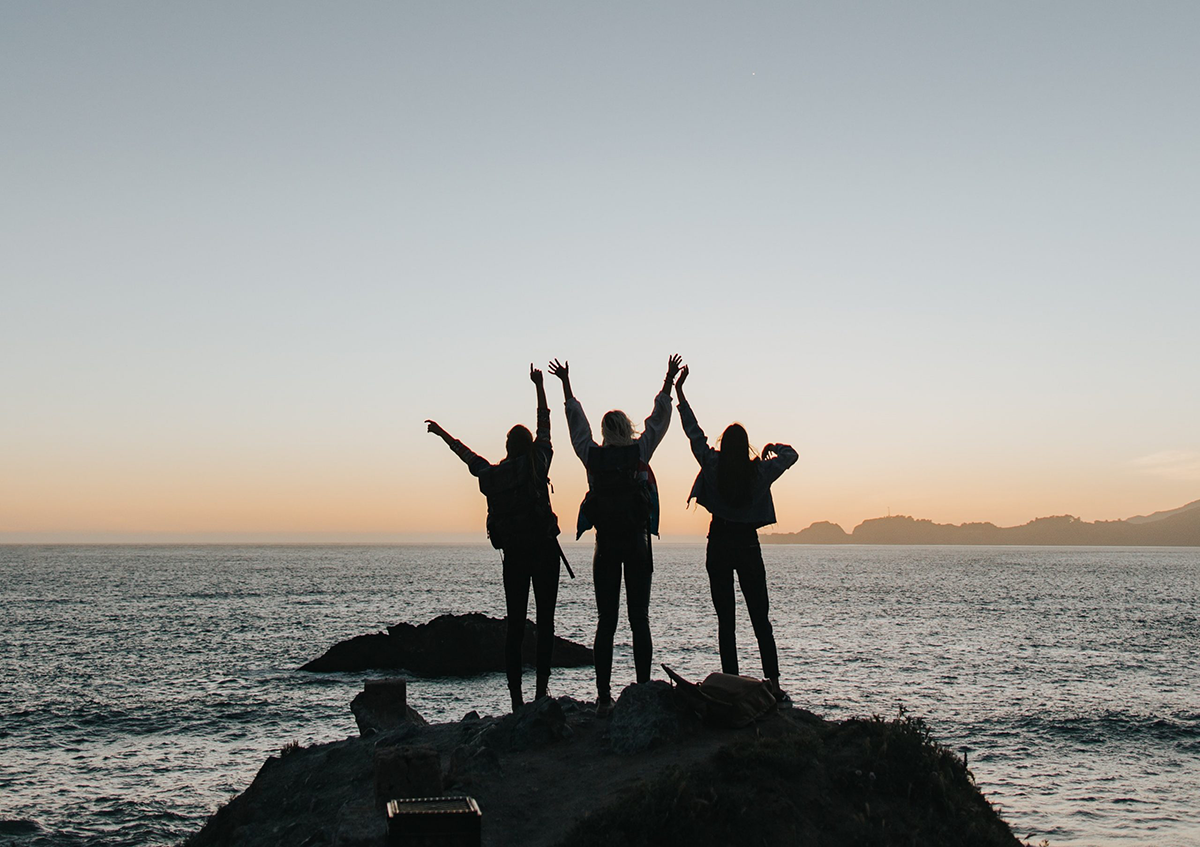 three people at the beach at sunset, there is a view of the ocean in the background and the people have their arms stretched towards the ski