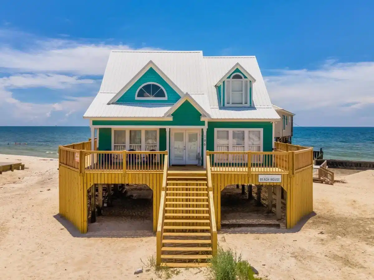 A beachfront home that i s teal with white trim located on the sands of Dauphin Island. This home is an affordable vacation rental by Whimstay
