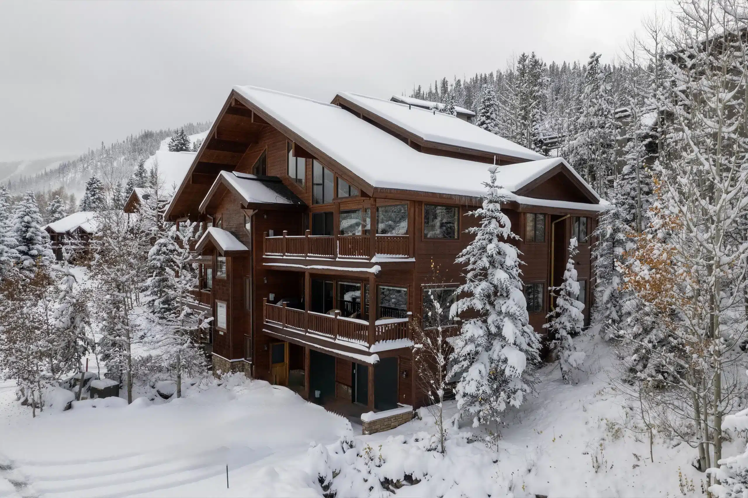 An affordable vacation rental cabin covered in snow with views of snow covered forest in the background