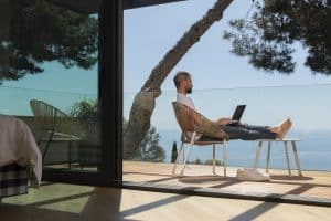 Man sitting on balcony with laptop overlooking the ocean.