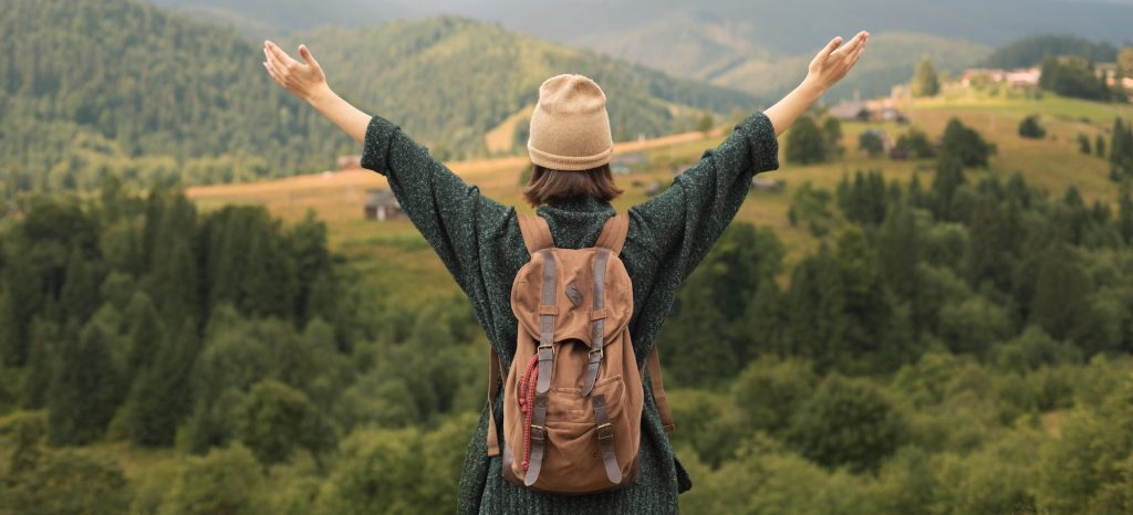 Traveler standing in front of vast landscape with outstretched arms.