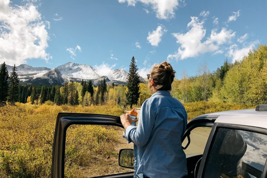 A female standing near the car enjoying the view with trees.