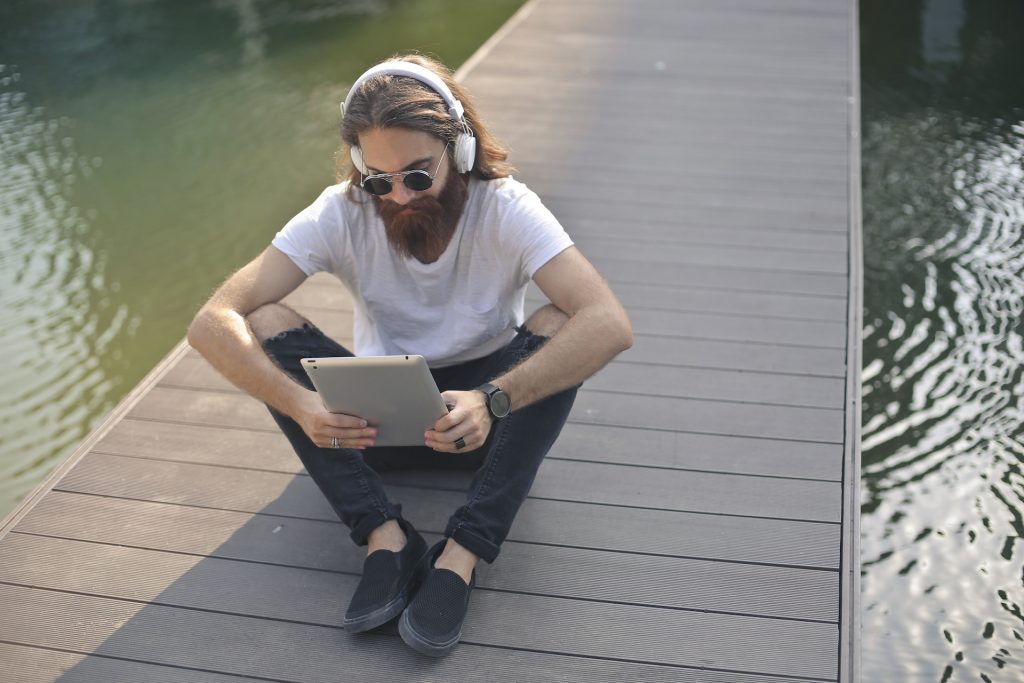 Man sitting on a pier near the water with his laptop.