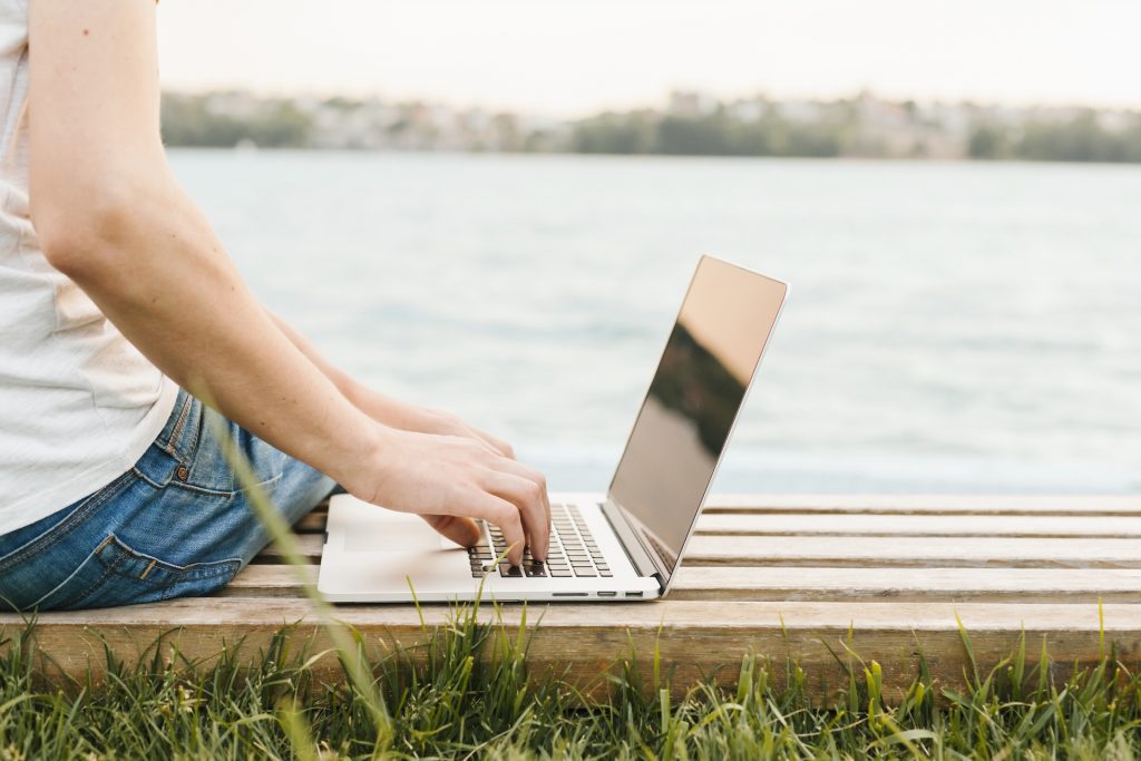 Man sitting on bench next to water with laptop.