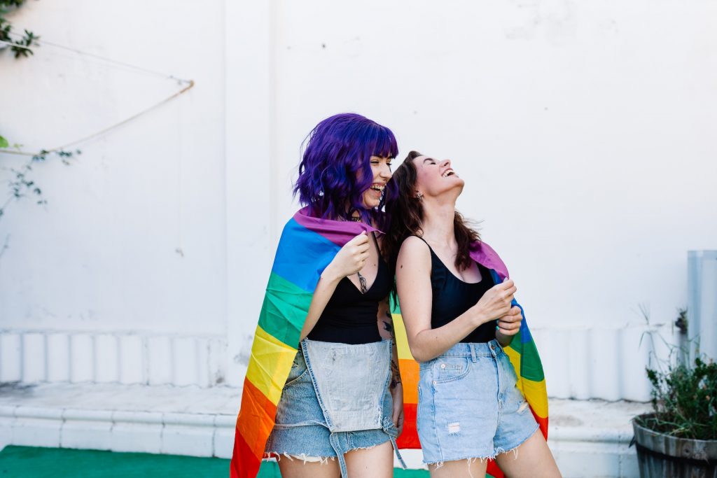 Two women wrapped in a rainbow flag.