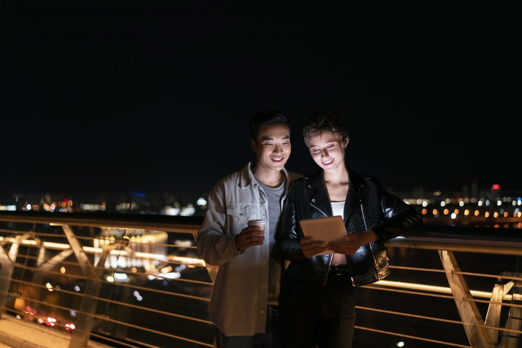 A couple looks at a tablet outside at night.