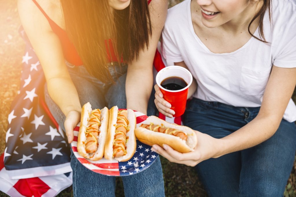 girls hold hotdogs at a Fourth of July parade.