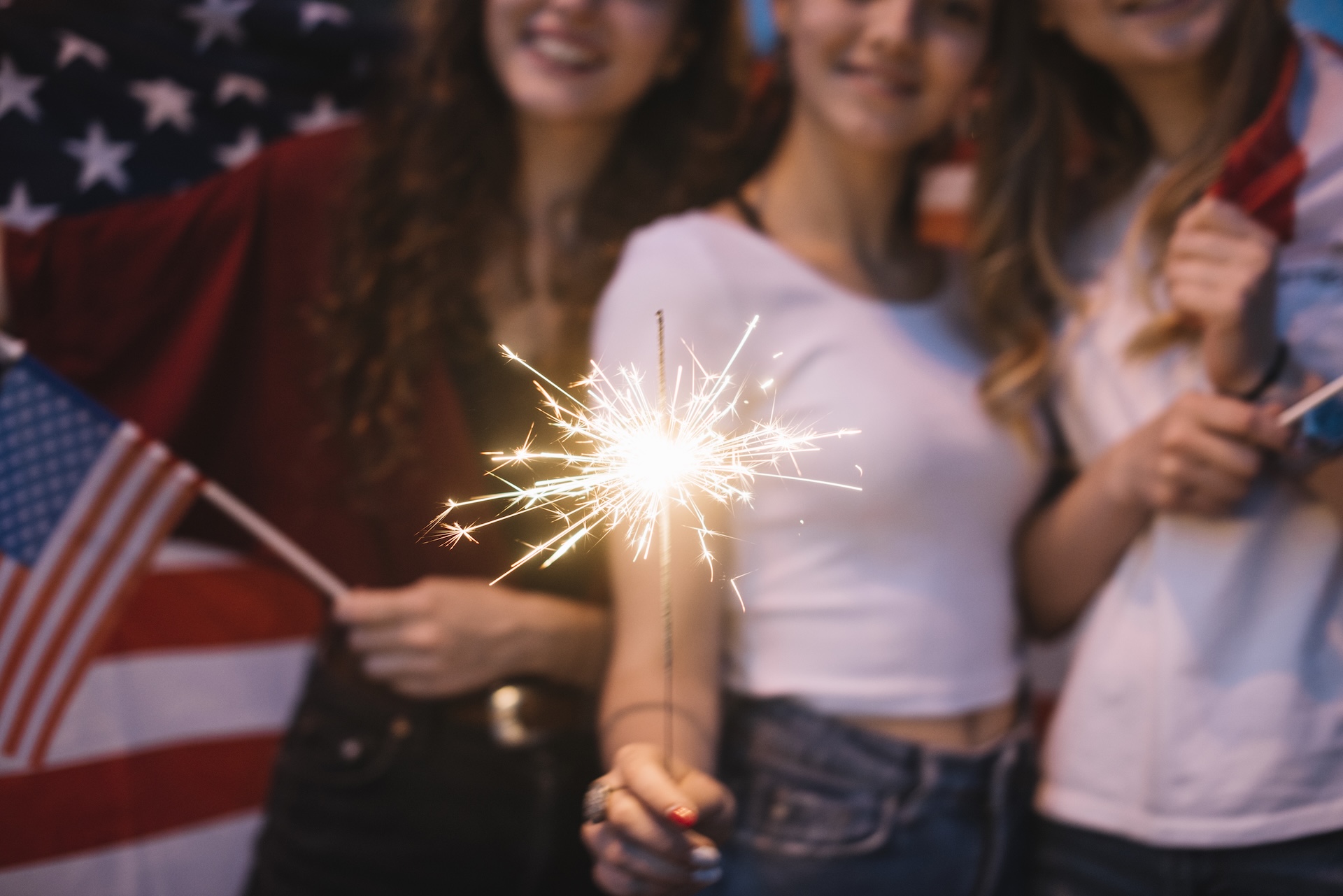 Girls holding a sparkler and American flag.